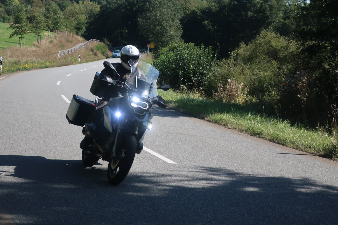 Motorrad auf einer sonnigen Landstraße zwischen Wiesen und Wald